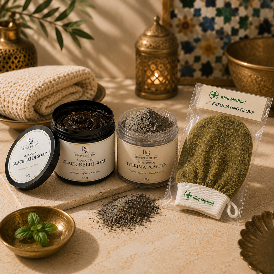 A styled flat-lay of three skincare products from Kiss Medical on a beige stone surface: a jar of black beldi soap, a jar of tebrima powder, and a packaged exfoliating glove, with loose powder spilled in front and decorative brass bowls and a folded cream towel in the background.
