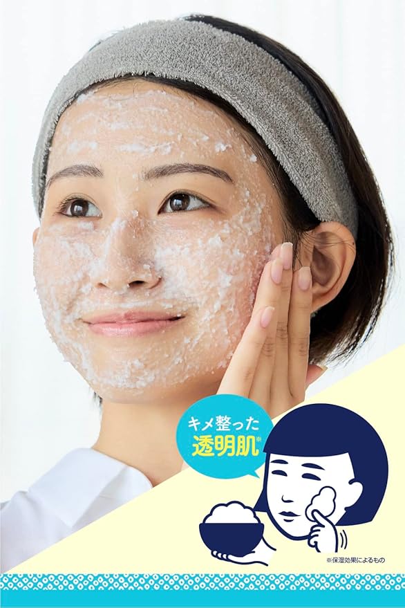 Woman applying a facial mask with a towel on her head, against a white background.