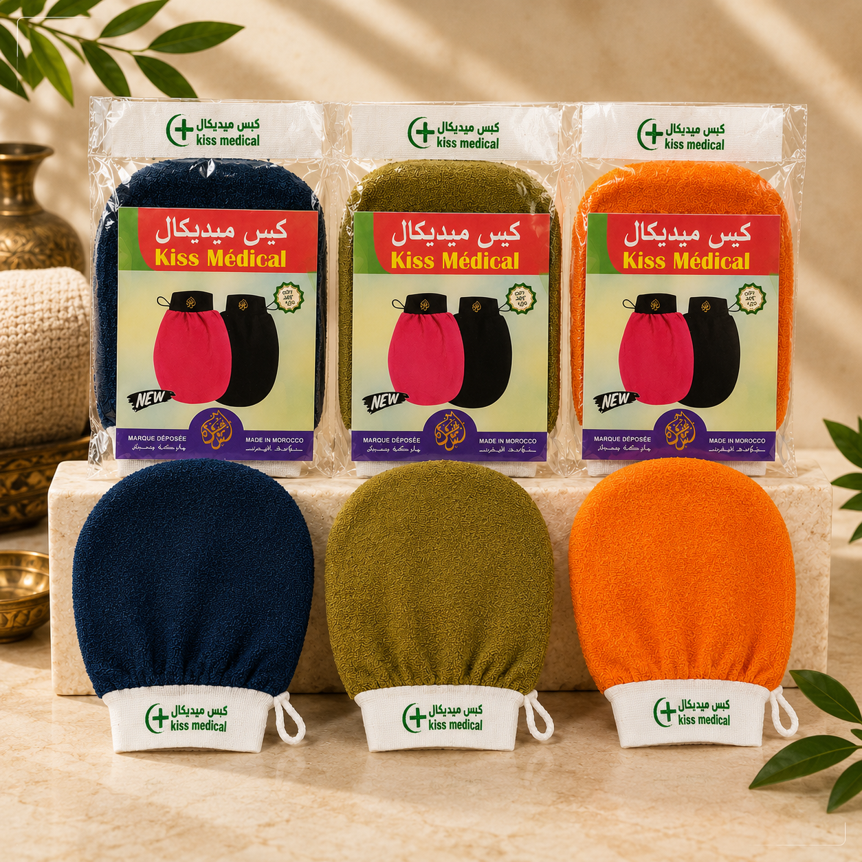 Three packaged Kiss Medical Kessa Gloves facial cleansing swabs in navy, olive green, and orange, displayed above their corresponding unpackaged swabs on a beige stone surface with decorative leaves and a brass vessel in the background.