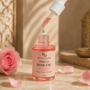 A bottle of Revive & Glow Moroccan Rose Oil with a dropper above it, set on a stone surface with pink rose petals and a pink rose in the background.