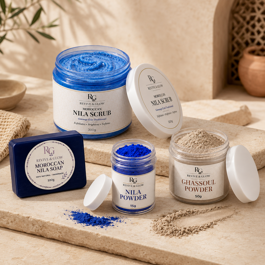 A set of Moroccan skincare products from Revive & Glow, including a blue nila scrub in a large jar, blue nila powder in a small jar, and beige ghassoul powder in another jar, alongside a dark blue soap bar, arranged on a beige stone slab.